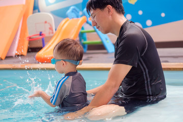Cute little Asian 2 years old toddler boy child in swimming costume learn to swim at indoor salt...