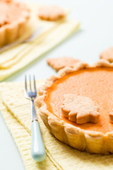 Pumpkin pie with cinnamon and cookies on yellow napkins on pastel blue background with autumn yellow leaves.