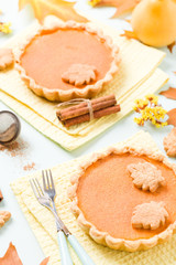 Pumpkin pie with cinnamon and cookies on yellow napkins on pastel blue background with autumn yellow leaves.