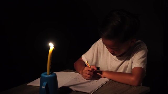 4k young Asian poor boy do homework under a candle light without electricity.