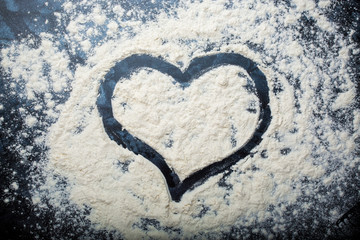 drawing a heart on a scattered flour on a dark background