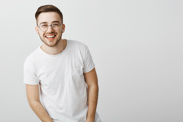 Portrait of happy friendly-looking stylish caucasian guy in glasses and wireless earphones laughing and smiling broadly squinting at camera from delight and positive emotions listening favorite music