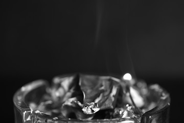 A piece of paper burning in a glass ashtray close up. Black and white