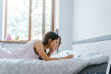 Beautiful young girl lies on a bed and writes something in the diary