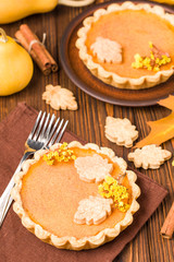 Pumpkin pie with cinnamon and cookies on brown napkins on wooden background with autumn yellow leaves.