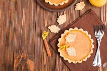 Pumpkin pie with cinnamon and cookies on brown napkins on wooden background with autumn yellow...