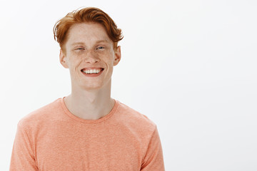 Horizontal shot of charming confident redhead young man with freckles and bright smile, grinning and gazing joyfully at camera, having fun and chilling with friends, being friendly and carefree