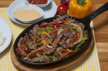 beef fajitas with colorful bell peppers in pan and sauces