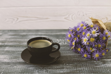 Romantic background with a cup of coffee, a bouquet of purple flowers in craft paper on a gray wooden table