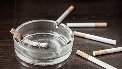 A glimmering cigarette burns in an ashtray on a table