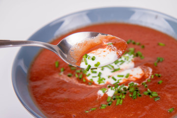 Beetroot cream soup decorated with yogurt and chives being eaten with a spoon
