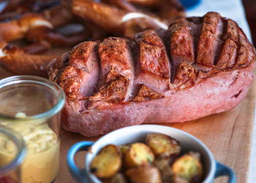 Frischer ganzer bayerischer Leberk&auml;se aus dem Ofen mit Bratkartoffeln Senf und Ketchup auf einem Holzbrett im Biergarten Wirtshaus Restaurant
