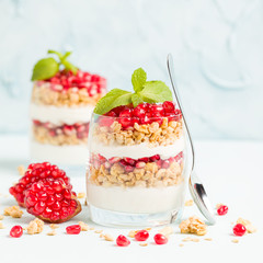 Pomegranate parfait - sweet organic layered dessert with granola flakes, yogurt and red ripe fruit seeds.