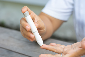 Close up of asian woman hands using lancet on finger to check blood sugar level by glucose meter, Healthcare medical and check up, diabetes, glycemia, and people concept