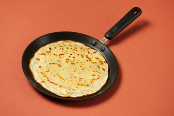 Crepe closeup, thin pancake on a frying pan, brown background
