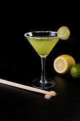 yellow cocktail with slice of lemon, chopsticks, lime and lemon on black background