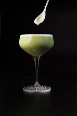 Milky cocktail stirred by cocktail spoon on black background