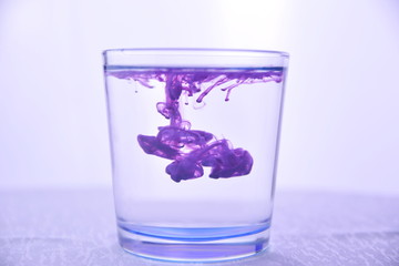 Glass with water on a white background with purple paint