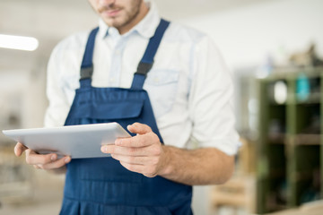 Young man in workwear holding touchpad while searching for ideas for new technical project