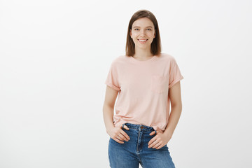 Good-looking optimistic and carefree european woman in casual t-shirt and jeans, holding hands in pockets and smiling broadly at camera, posing for advertisement, talking casually with friends