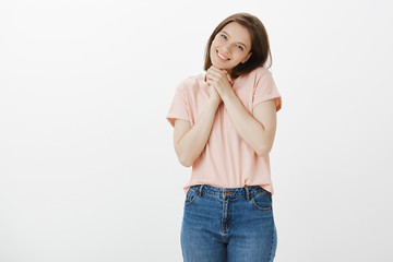 You are so cute I am touched. Portrait of pleased charming woman in trendy t-shirt, tilting head and smiling broadly, clenching hands together while being moved with pleasant surprise