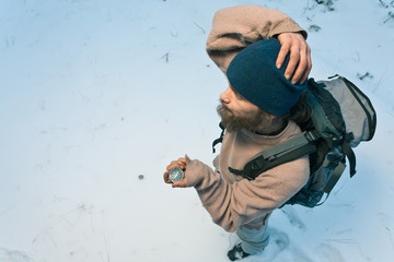 bearded confused traveller with compass in winter forest tries to find his way, top view