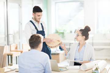 Young cabinetmaker showing experts one of wood samples while discussing its characteristics at meeting