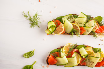Sliced trout (salmon) fish sandwich with ogerets, rye bread and dill on white background.
