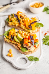 Vegan healthy sandwiches with hummus, chickpeas, baked vegetables and basil on white board.
