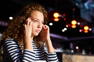 Tired or tense woman with wavy hair touching her temples while trying to concentrate