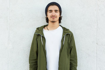Horizontal shot of stylish teenage boy wears black hat, white t shirt and green anorak, looks with...