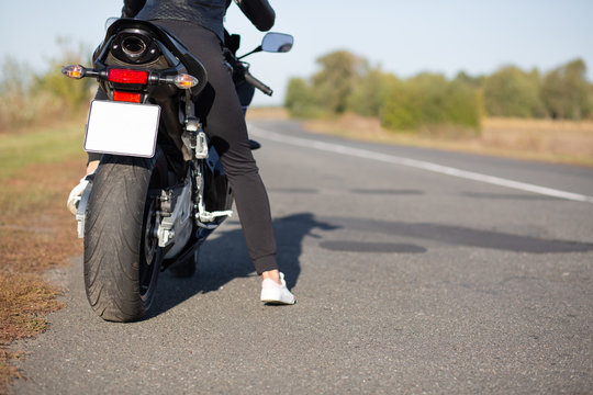 Cropped image of unrecognizable female bikes poses back on bike at asphalt, wears black clothes, blank copy space aside for your advertisement or promotional text. People, transport, destination