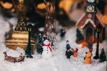 Magic Little Christmas city in miniature with snow,snowman, lights, people and children toys, trees and old building. Stylish christmas decorations in window. Festive decor, winter holidays