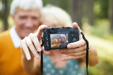 Digital photocamera in hands of senior female making shot of her husband and herself