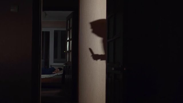 Shadow on the wall of a masked robber with a knife in his hand