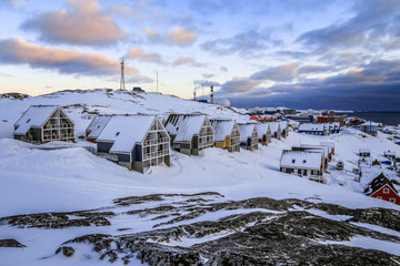 Rows of colorful Inuit houses hiding in the snow and rocks with fjord in the background, suburb of arctic capital Nuuk, Greenland