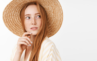 Curious thoughtful charming ginger girl with cute freckles in trendy summer straw hat turning right...