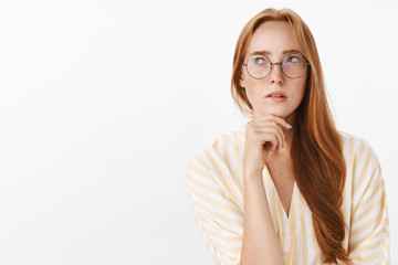 Woman remembering schedule while planning next work day standing focused and perplexed in trendy glasses looking at upper left corner thoughtful and concentrated making calculations in mind