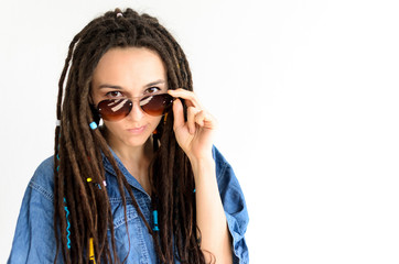 girl with dreadlocks in a blue shirt looks into the camera over sunglasses