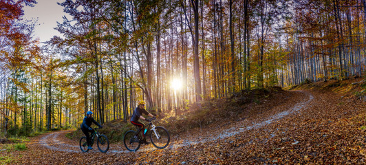 Cycling, mountain biker couple on cycle trail in autumn forest at sunset. Mountain biking in autumn...