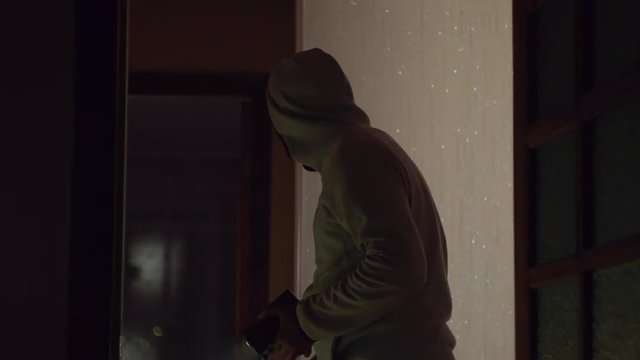 Masked burglar with flashlight in someone apartment