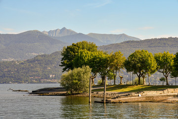 Veduta di un'isola in mezzo ad un lago con fila di alberi e montagne sullo sfondo in estate, Isola dei Pescatori, Lago Maggiore, Piemonte, Italia