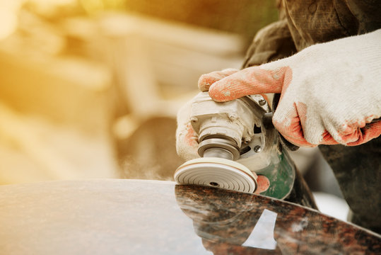 close-up a man in gloves polishes a marble monument with an angle grinder on a blurred background. grinding stone.