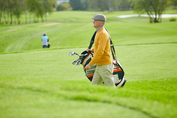 Obraz premium Side view of mature man in casualwear carrying bag with golf clubs while hurrying for game