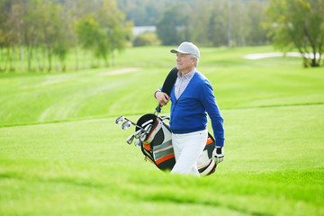 Obraz premium Senior man in casualwear walking for game of golf and carrying clubs in bag