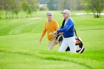 Poster Twee oude vrienden praten terwijl ze zich haasten voor een partijtje golf langs het groene veld © pressmaster