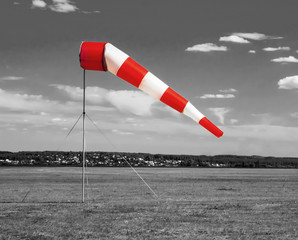 Red and white windsock wind sock  on the aerodrome, monochrome black and white field, sky and clouds background