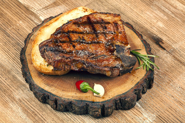Piece of bone steak on wooden board with a branch of rosemary.