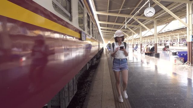 Slow motion - Traveler backpacker Asian woman travel in Bangkok, Thailand. Happy young female using smartphone for talking, reading and texting at train station.