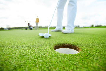 Obraz premium Golf player holding club close to the ball before hitting it while targeting at hole